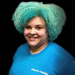 woman with short curly blue hair wearing a blue merry maids tshirt standing in front of a black photo backdrop
